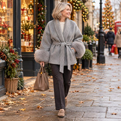 A woman wearing the Dianne Belted Wrap Coat with Faux Fur Cuffs in Grey